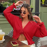 Woman in a red cardigan sitting outdoors with a drink and phone on a table.